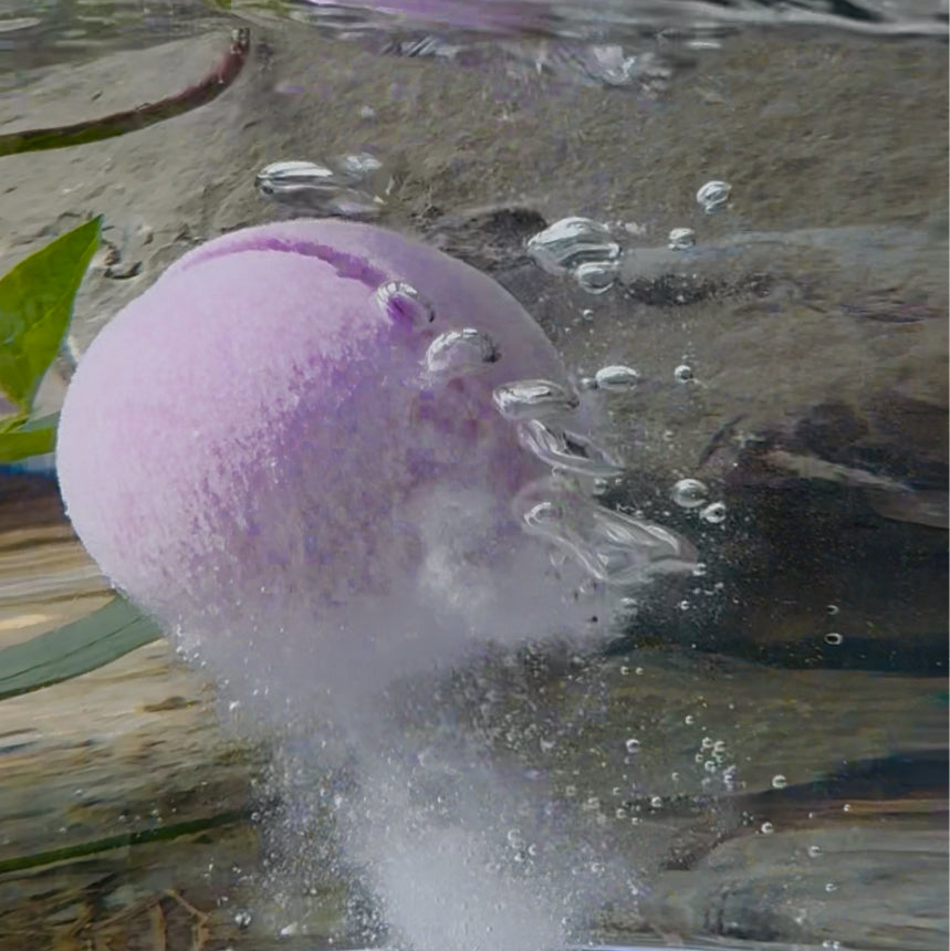 Purple bath bomb bursting in water with bubbles and leaves in the background