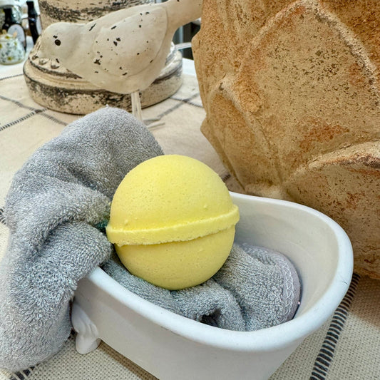 Yellow bath bomb in a small white bathtub with gray towels on a patterned surface